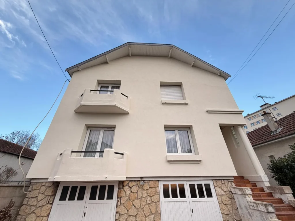 Façade de maison avec balcons et soubassement en pierre, finie sous enduit beige
