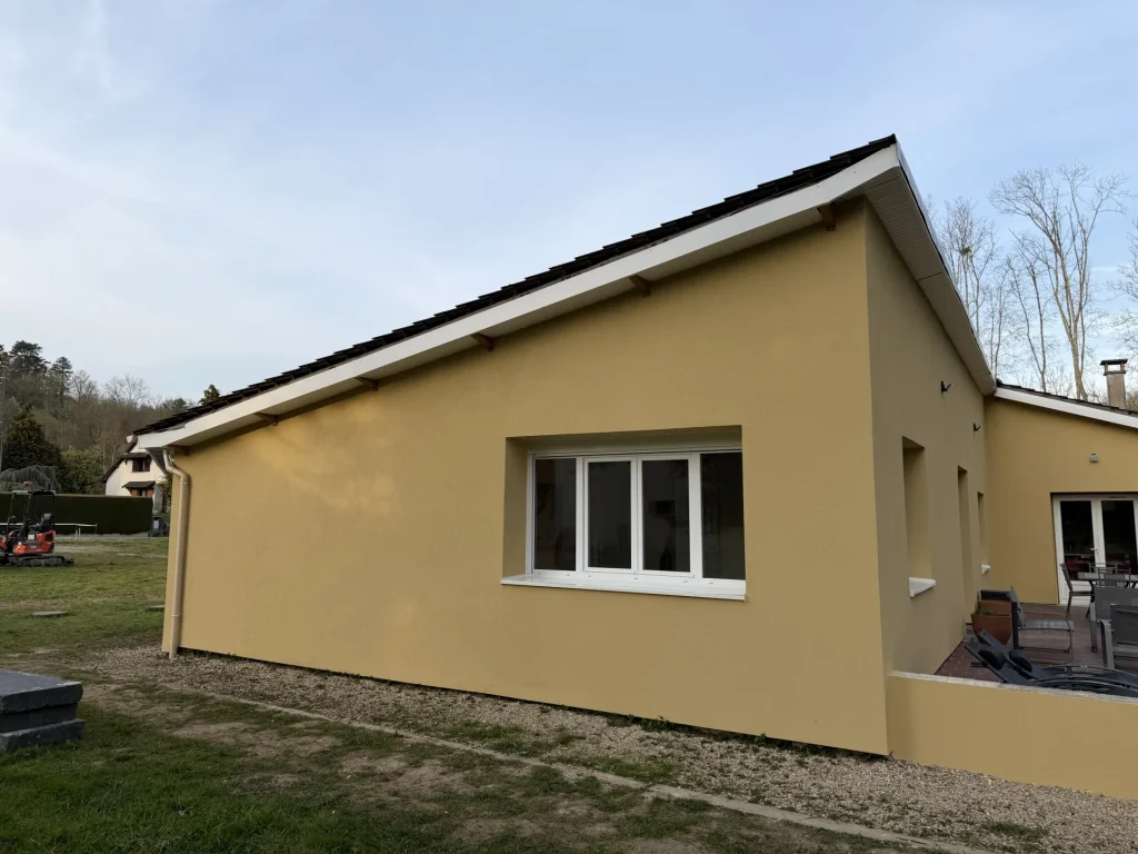 Pignon d’une maison de plain-pied isolé par l’extérieur, enduit ocre et fenêtre en applique